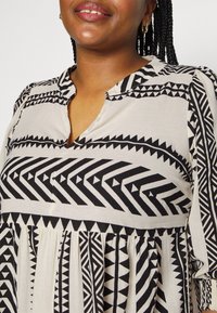 Blusa de estampado en blanco y negro con diseños geométricos, escote con tapeta y tela fruncida en la cintura.