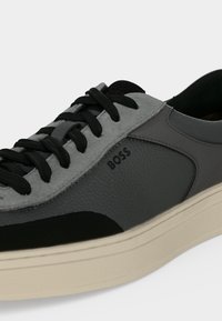 Gros plan d'une basket grise et noire à lacets en cuir texturé, logo BOSS sur le côté, et semelle épaisse couleur blanc cassé.