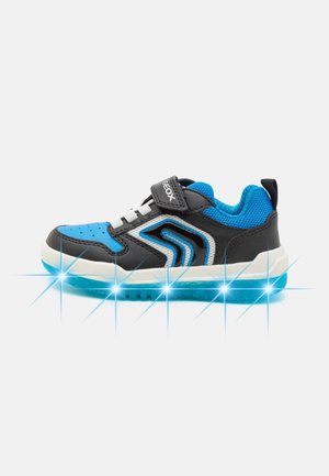Dziecięcy niebiesko-czarny sneaker z białymi sznurowadłami, paskiem na rzep i świecącą podeszwą na białym tle.