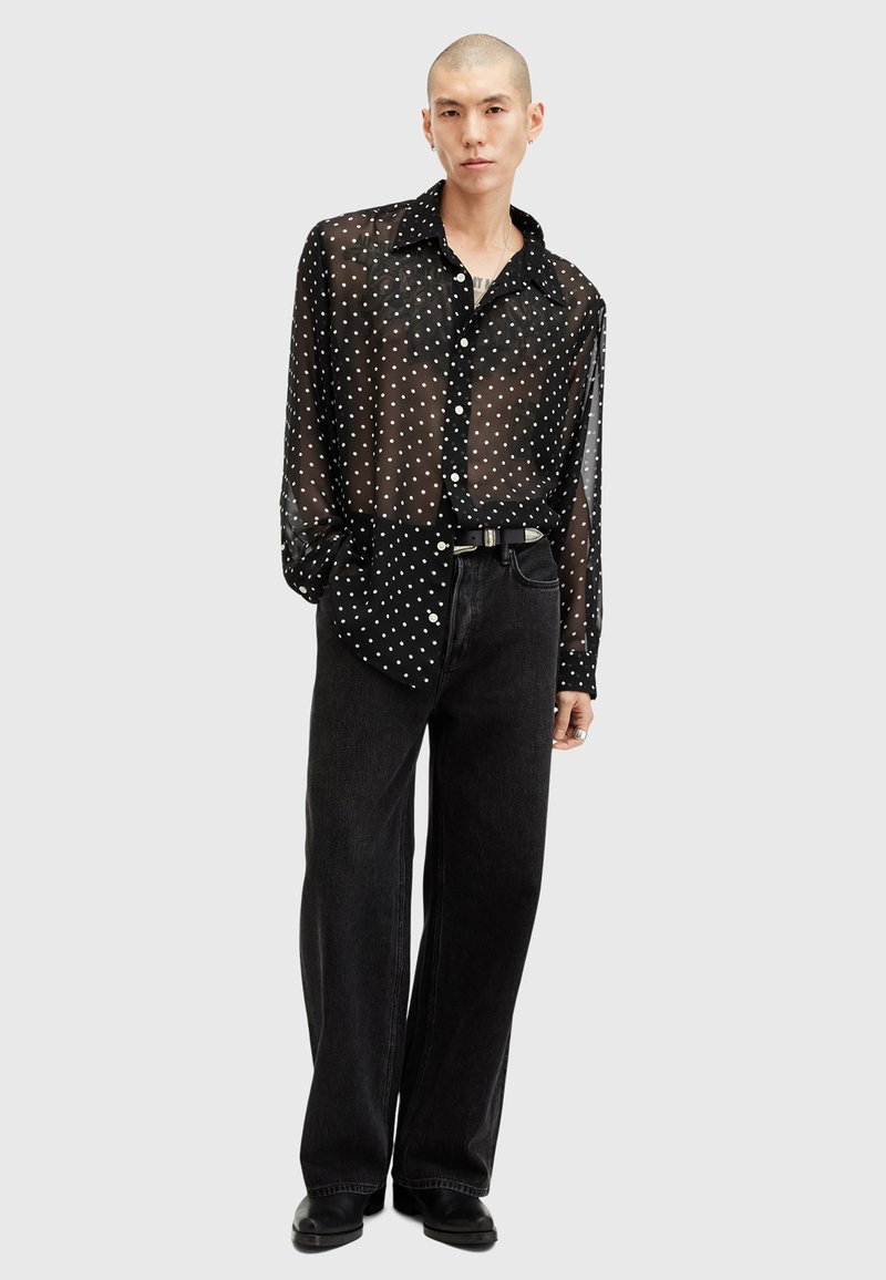 Zwarte doorschijnende button-up shirt met witte stippen, gecombineerd met hoge zwarte jeans. Soepele textuur, relaxte pasvorm en lange mouwen.