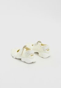 White mesh sneakers with a textured design, featuring Velcro straps, rounded soles, and open sides for breathability.