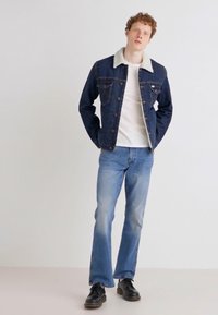Denim jakna z lahkim sivim krznim ovratnikom, temno modra tkanina, spredaj z gumbi. V kombinaciji z svetlo modrimi kavbojkami in črnimi čevlji. Enostaven dizajn.