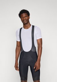 Shorts de cyclisme noirs avec un rembourrage au niveau de l'assise, associés à un t-shirt ajusté en maille texturée blanche. Comprend des bretelles ajustables et un design sans coutures.