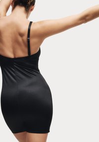 Vestido negro ajustado hecho de material liso y elástico. Presenta finas correas ajustables y una silueta estilizada.