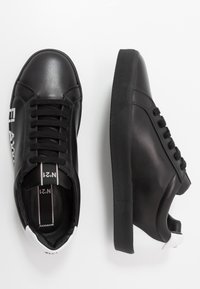 Un paio di sneakers in pelle nere basse con lacci neri, dettagli bianchi sul tallone e testo stampato bianco sul lato esterno di una scarpa.