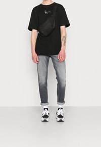 Černé volné tričko, šedé džíny s postupným blednutím, černá ledvinka a bílo-černé tenisky s polstrovanými detaily.