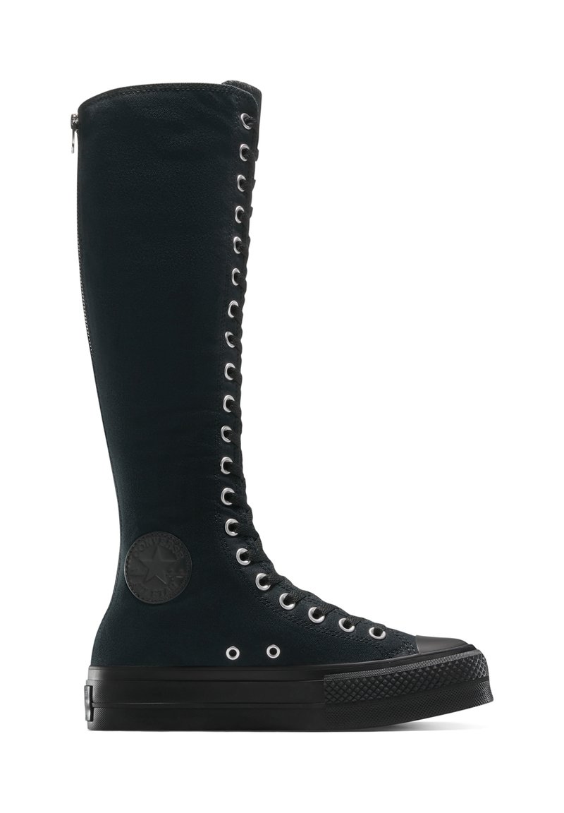 Schwarze Wildleder-Hochschaftstiefel mit Metallösen, Reißverschlussdetails und einem kreisförmigen Markenpatch an der Seite. Dicke Gummisohle und strukturierte Oberfläche.
