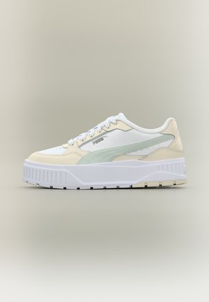 Baskets Puma blanches et beiges avec une bande vert clair, semelle blanche épaisse et lacets blancs sur fond neutre, vue de côté.