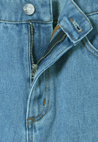Tissu en denim bleu clair, avec une fermeture éclair argentée et un bouton. Couture en fil contrastant beige. Vue en gros plan de la taille.