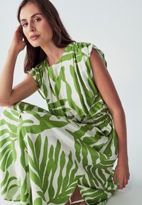 Zelena i bijela haljina s uzorkom lišća, do sredine tele, s kratkim rukavima i elastičnim strukom za opušteni kroj.