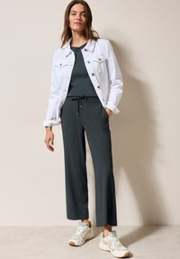 Veste en denim blanche, haut vert foncé, pantalon large texturé et baskets avec des accents menthe. Tenue décontractée avec des matériaux mélangés et une coupe relax.