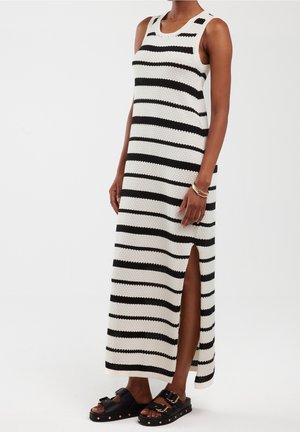 Henkilö, jolla on päällään mustavalkoisin vaakaraitakuosin hihaton maksimimekko, jossa on sivuhalkio, ja mustat solkikengät.