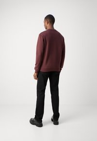 Felpa borgogna con collo a giro, texture morbida, polsini e orlo a coste, abbinata a pantaloni neri a vestibilità dritta e calzature nere.