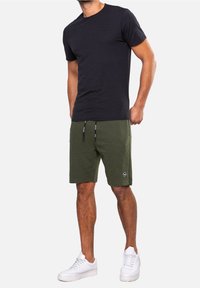 T-shirt noire à manches courtes associée à un short rayé vert et des baskets blanches. Le short comporte un cordon de serrage et un détail de patch logo.