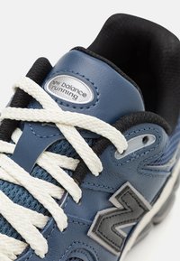 Scarpa da corsa in pelle blu con lacci bianchi, dettagli in rete e logo "N" grigio. Presenta un colletto imbottito e una superficie testurizzata.