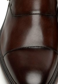 Zapato de cuero marrón con un acabado suave, con puntera redondeada, detalles de costura a lo largo de la parte superior y una textura pulida.