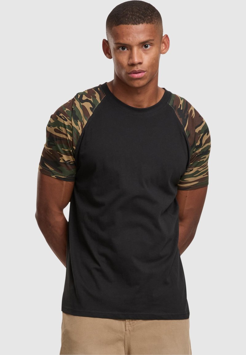 Black t-shirt with camo patterned raglan sleeves. Smooth fabric, fitted design, round neckline, and short sleeves. No visible logos or graphics.