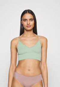 Top court en mailles vert clair avec des bretelles fines et un décolleté en V, associé à un bas de bikini rose pâle, sur un fond uni.