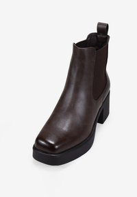 Bottines en cuir marron avec des panneaux latéraux élastiques, bout carré et talon bloc. Texture lisse avec des détails de couture minimaux.