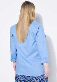 Helles blaues Hemd mit hochgerollten Ärmeln, weichem Baumwollmaterial, knopflosem Design und geradem Schnitt, von hinten präsentiert.