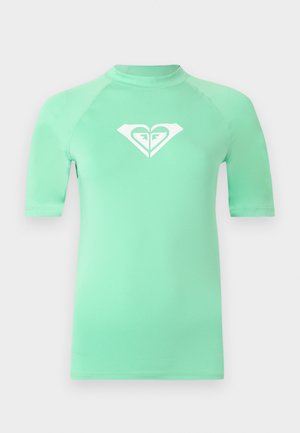 Bluză de protecție mint cu mâneci scurte, cu logo alb în formă de inimă pe piept, având guler înalt și cusături adaptate.