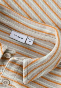 Randig polo i mjukt material. Har orange och ljusblå ränder, krage med knappar och en etikett märkt "name it" med storleksinformation.