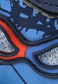 Zapato de goma azul con superficie texturizada, que presenta acentos rojos y detalles translúcidos. El patrón se asemeja a un diseño estilizado.