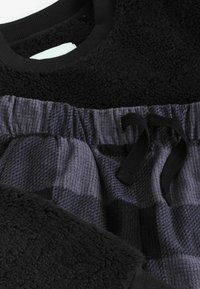 Czarny polarowy sweter z ryżowym dekoltem, w połączeniu z ciemnoszarymi i czarnymi spodniami w kratę z regulowanym paskiem w talii.