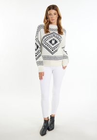 Maglione bianco con motivi geometrici neri, polsini a costine e scollo a girocollo, abbinato a jeans skinny bianchi e stivali alla caviglia neri.