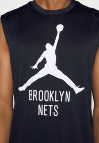 Mouwloze zwarte shirt met witte silhouet van een springende basketbalspeler die een bal vasthoudt, met de tekst "Brooklyn Nets" onder de afbeelding.
