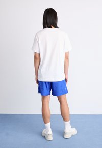 Hvid bomulds T-shirt med korte ærmer, parret med blå træningsshorts. Hvide sneakers og synlige hvide ankelstrømper. Simpelt design.