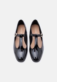 Μαύρα παπούτσια από δερμάτινο γυαλιστερό δέρμα με σχέδιο T-λουρί, στρογγυλεμένη μύτη και χρυσή πόρπη. Λείο υφή και μίνιμαλ αισθητική.