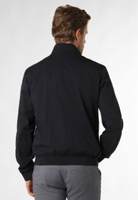 Giacca bomber nera da uomo, tessuto leggero, polsini e orlo a coste, colletto classico, texture liscia, design minimalista, senza accentuazioni visibili.