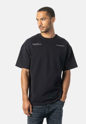 Sort kortærmet t-shirt lavet af bomuld, med rund halsudskæring og hvide teksttryk på forsiden, parret med blå denimjeans.