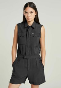 Jumpsuit nero senza maniche con colletto, zip frontale, due tasche sul petto e vita con cintura. Tessuto testurizzato con una vestibilità comoda.