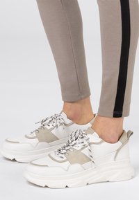 Sneaker chunky bianchi e beige in pelle e suede testurizzata. Lacci a strisce black e white. Indossati con leggings beige con una striscia nera.