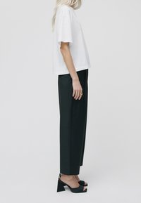 Camiseta blanca corta, pantalones de pierna ancha negros y sandalias de tacón abiertas negras. Tejido liso y suave, con un ajuste relajado y un diseño minimalista.