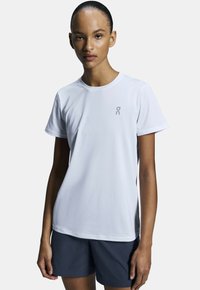 Vit T-shirt med kort ärm för träning, rund halsringning och en liten grå logotyp på bröstet, tillverkad av ett mjukt, fukttransporterande material.
