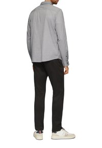 Camicia a maniche lunghe grigia a motivi con polsini a bottone, abbinata a pantaloni neri e sneakers di colore chiaro. Inquadratura sul retro e design semplice.