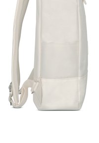 Oldalnézet egy bézs szövet hátizsákról, amelyen párnázott vállpántok és egy kis külső zseb látható.