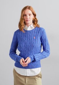 Sinise tikk-kudumine, ümmarguse kaelusega kampsun, millel on soonikkrae ja -ääred, ning vasakul rinnal väike tikand. Kantud valge kraega särgi peal.