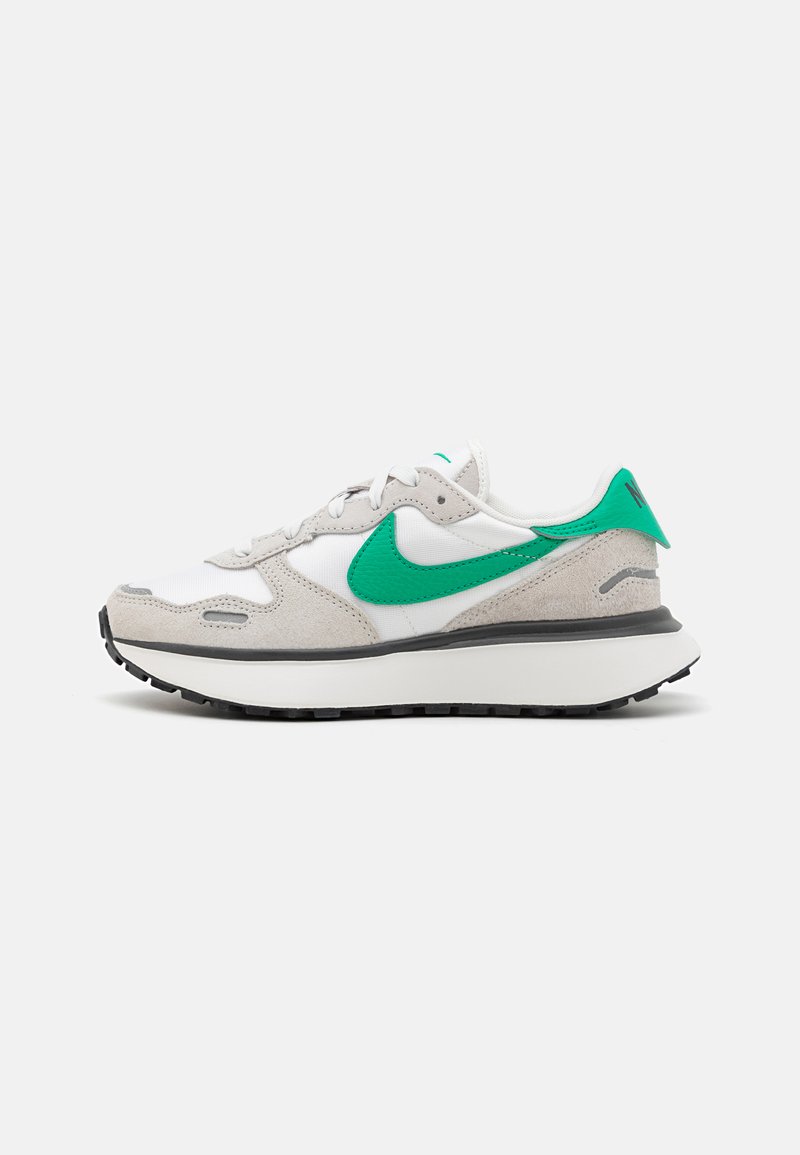 Zapatillas blancas y grises con un swoosh verde de Nike, parte superior de ante y malla, cuello acolchado y suela de goma con patrón de tracción.