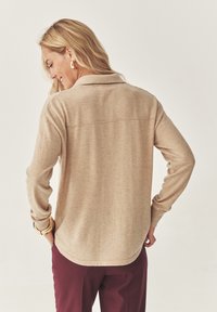 Pullover beige in maglia con collo a polo, maniche lunghe e orlo curvo. La texture sembra morbida e liscia.