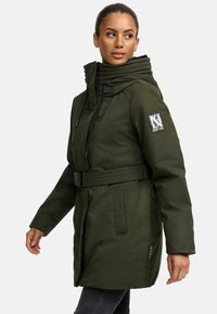 Parka verte à capuche avec une taille ceinturée, fermeture éclair devant, poches latérales et un badge à motif sur le bras gauche. Finition en tissu texturé.