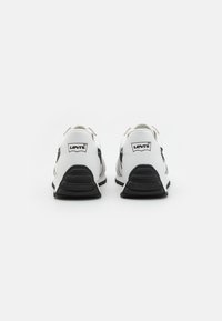 Weiße und schwarze Sportschuhe mit einem strukturierten Stoffobermaterial, Gummisohle und markierten Fersenschlaufen. Die Rückansicht zeigt kontrastierende Designelemente.