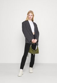 Blazer oversized riscado a preto, top cropped branco, calças pretas justas, bolsa satin verde, ténis brancos. Design simples com acentos mínimos.