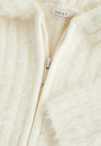 Felpa zip-up di colore crema realizzata in un morbido tessuto peloso. Presenta un design a coste con una zip bianca e un'etichetta "NEXT" all'interno del colletto.
