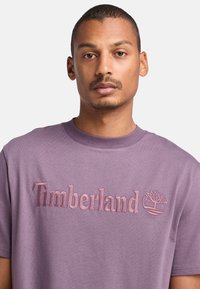 Fialové bavlněné tričko s vyšitým textem a logem 'Timberland'. Krátké rukávy a design s kulatým výstřihem s hladkou texturou.