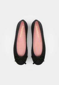 Paire de ballerines noires avec semelles roses et petits nœuds décoratifs sur les orteils, vues de dessus sur un fond clair.