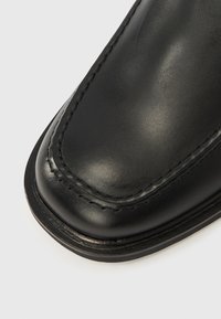 Zapato de cuero negro con acabado liso, punta redonda, costuras contrastantes y suela de perfil bajo. Diseño minimalista, bordes limpios.